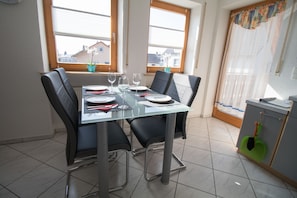 Un espace repas avec une table en verre, des chaises noires et une vue sur les bâtiments à travers les fenêtres.