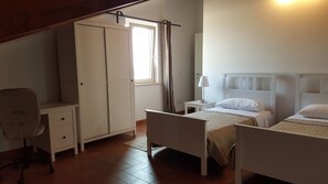 Un dormitorio con dos camas individuales, un escritorio, una silla, un armario y una ventana con cortinas.