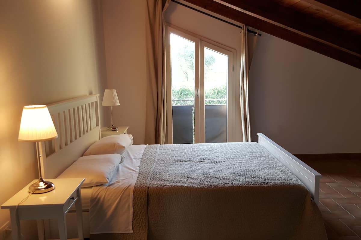 Ein Schlafzimmer mit einem Bett, einem Nachttisch, einer Lampe und einem Fenster mit Vorhängen.