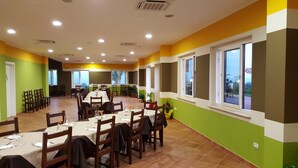 Un comedor con varias mesas y sillas, ventanas amplias y una decoración en tonos verde y amarillo.