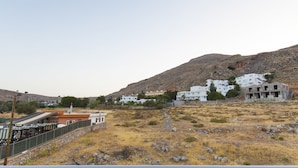 A residential area with white buildings, a rocky hillside, and a fenced area with a structure that appears to be a house or small building. - Lindos Portes Suites - Adults Only (Rhodes)