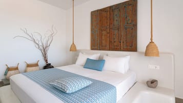 Een slaapkamer met een groot bed, wit beddengoed, een blauw gestreept plaid, een houten deur en twee hangende lampen.