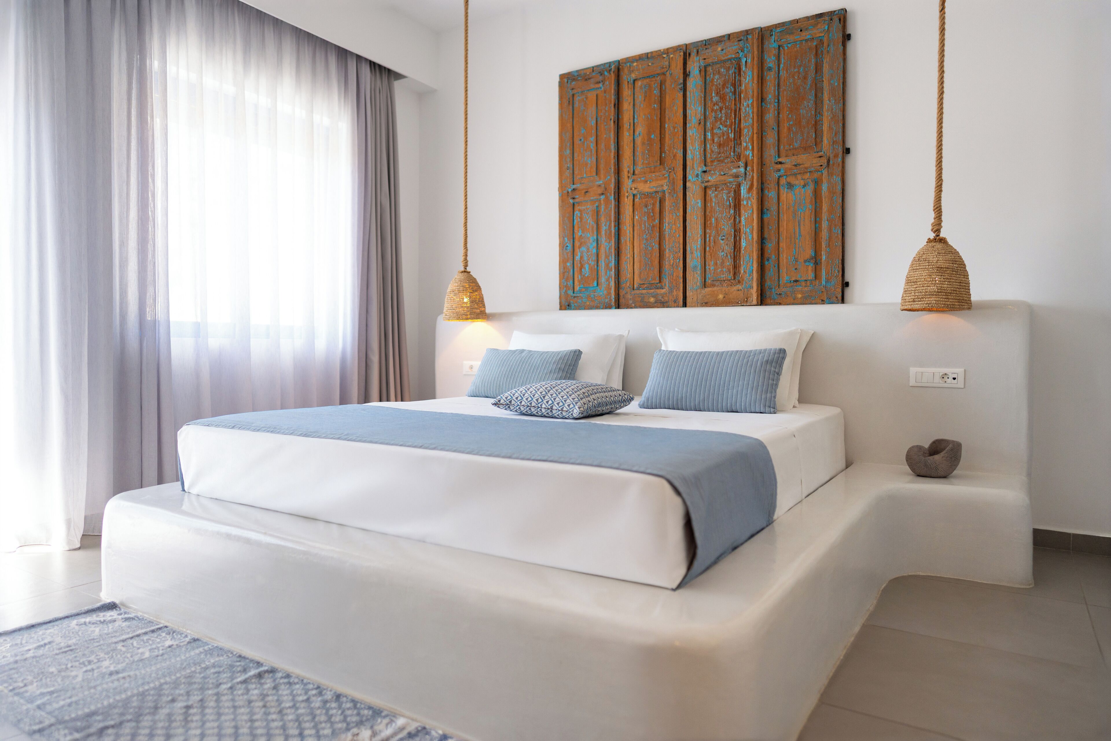 A modern bedroom with a large bed, two bedside lamps, and a decorative wooden panel above the bed.