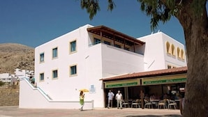 A white building with a covered outdoor seating area and a staircase leading to an upper level. - Lindos Portes Suites - Adults Only (Rhodes)