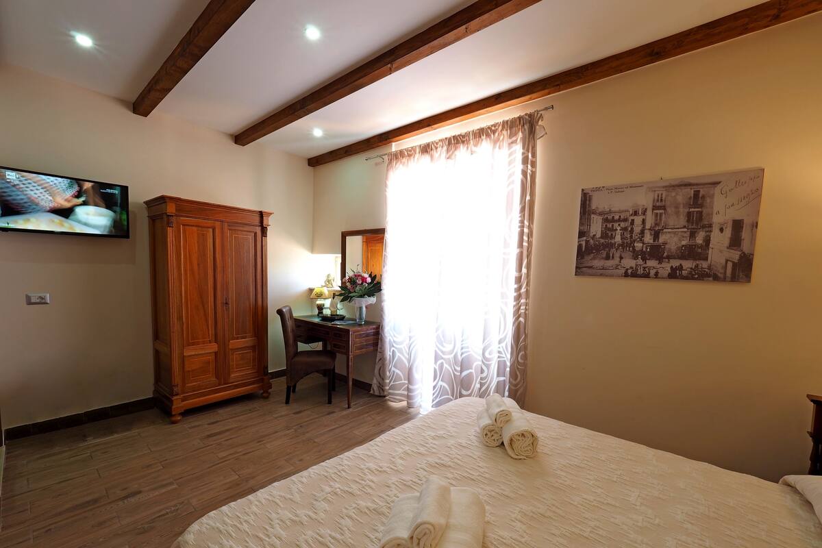 Un dormitorio con un escritorio de madera, televisor, armario y cama con toallas enrolladas.