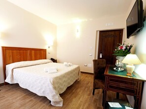 Ein Hotelzimmer mit einem Bett, einem Schreibtisch mit Lampe, einem Stuhl, einer Holztür und einem flachbildfernseher an der Wand.
