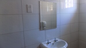 A bathroom with a white sink, a mirror, and a wall-mounted soap dispenser. - Etana Motel (Kampala)