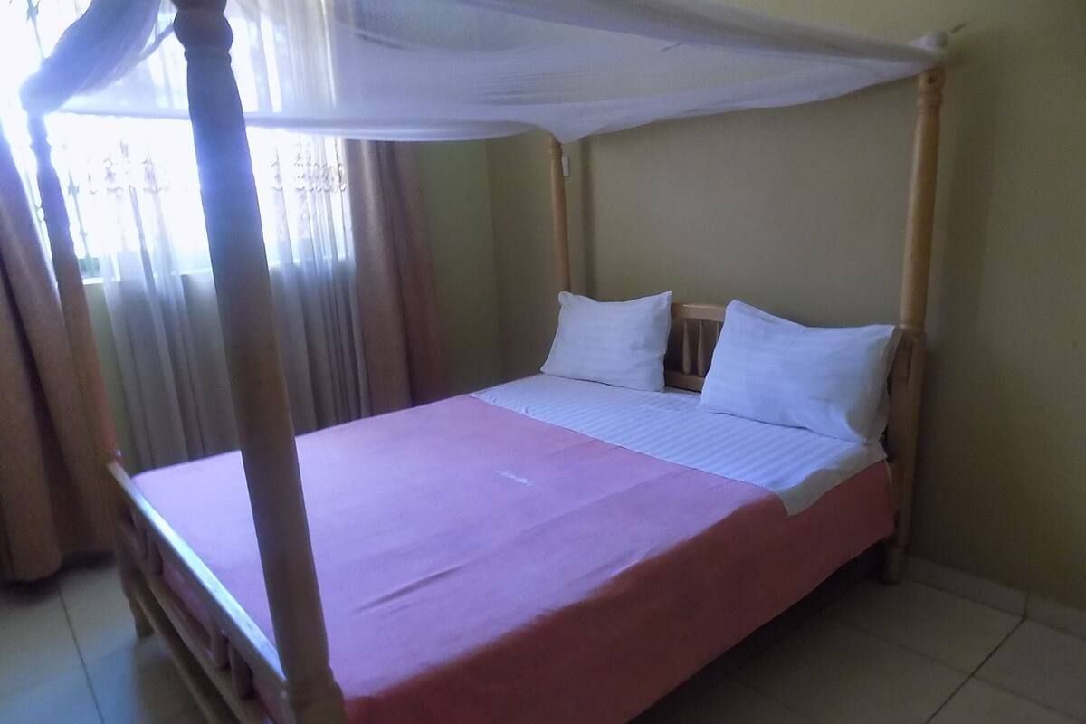 A four-poster bed with white linens, a wooden headboard, and a pink bedspread.