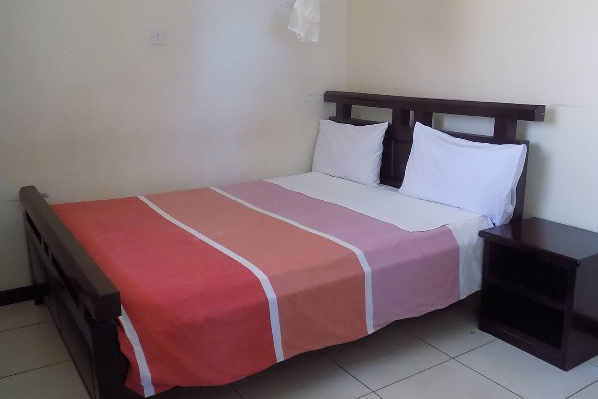 A single bed with a red and white striped bedspread, a wooden headboard, white pillows, and a dark nightstand.