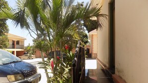 Una zona residencial con un coche estacionado en la calle, una escalera que lleva a un edificio y una palmera.