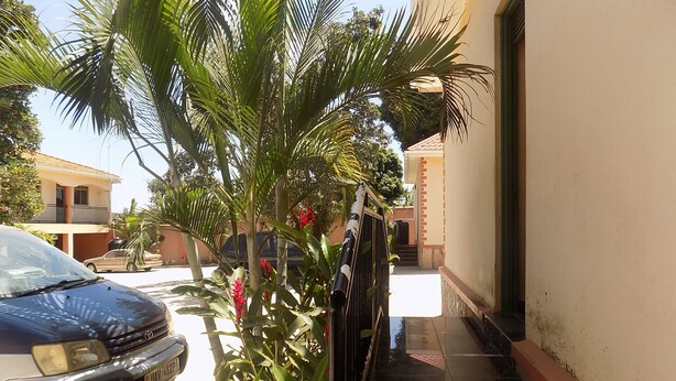 A residential area with a car parked on the street, a staircase leading to a building, and a palm tree. - Etana Motel (Kampala)