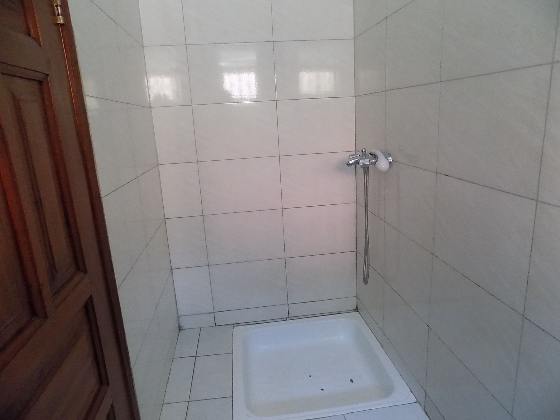 Un baño pequeño con azulejos, una ducha, una puerta de madera y una bañera blanca.