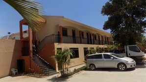 A multi-story building with a central staircase, balconies, and a parking area with a silver car and a white van. - Etana Motel (Kampala)