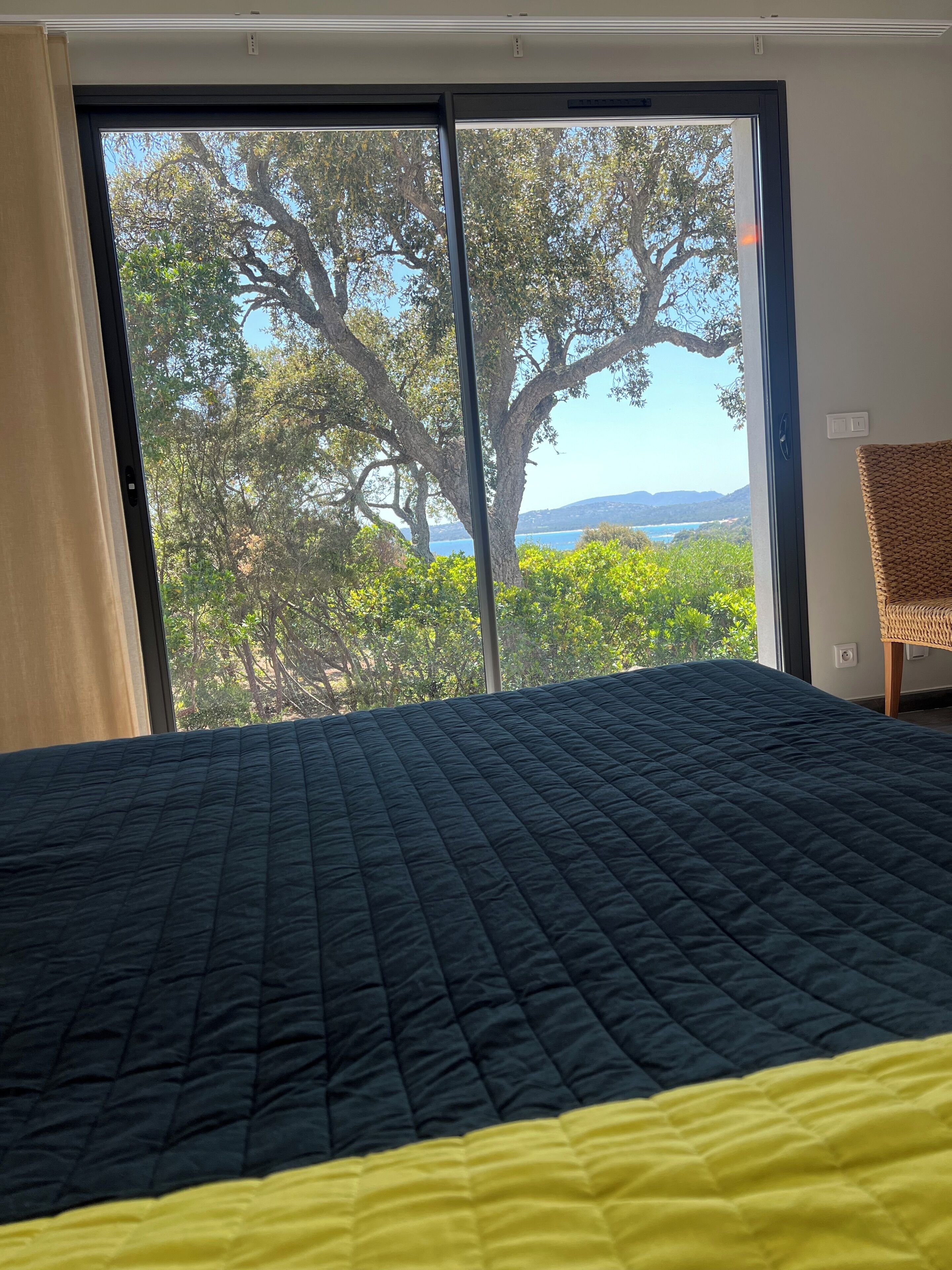 Quarto com cama grande, vista para árvores e um corpo de água por uma porta de correr.