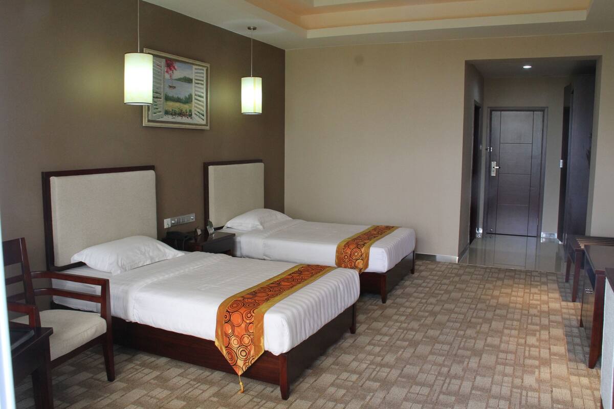 A hotel room with two single beds, a wooden chair, a desk, and a nightstand.