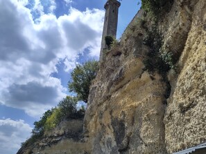 Un acantilado rocoso con una alta torre de piedra y vegetación escasa.