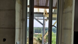 Une pièce dotée d’une grande fenêtre, d’une structure métallique à l’extérieur et d’un mur percé d’un trou.