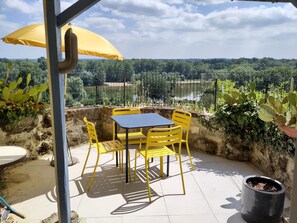 Un patio con sillas y una mesa amarillas, una sombrilla amarilla y vista a un lago y árboles.