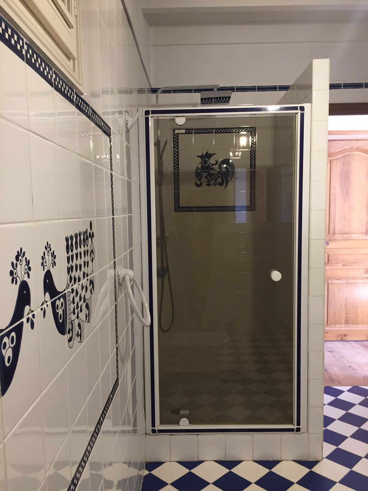 Et bruseområde med glasdør, flisevægge med dekorative mønstre og et skakternet gulv.