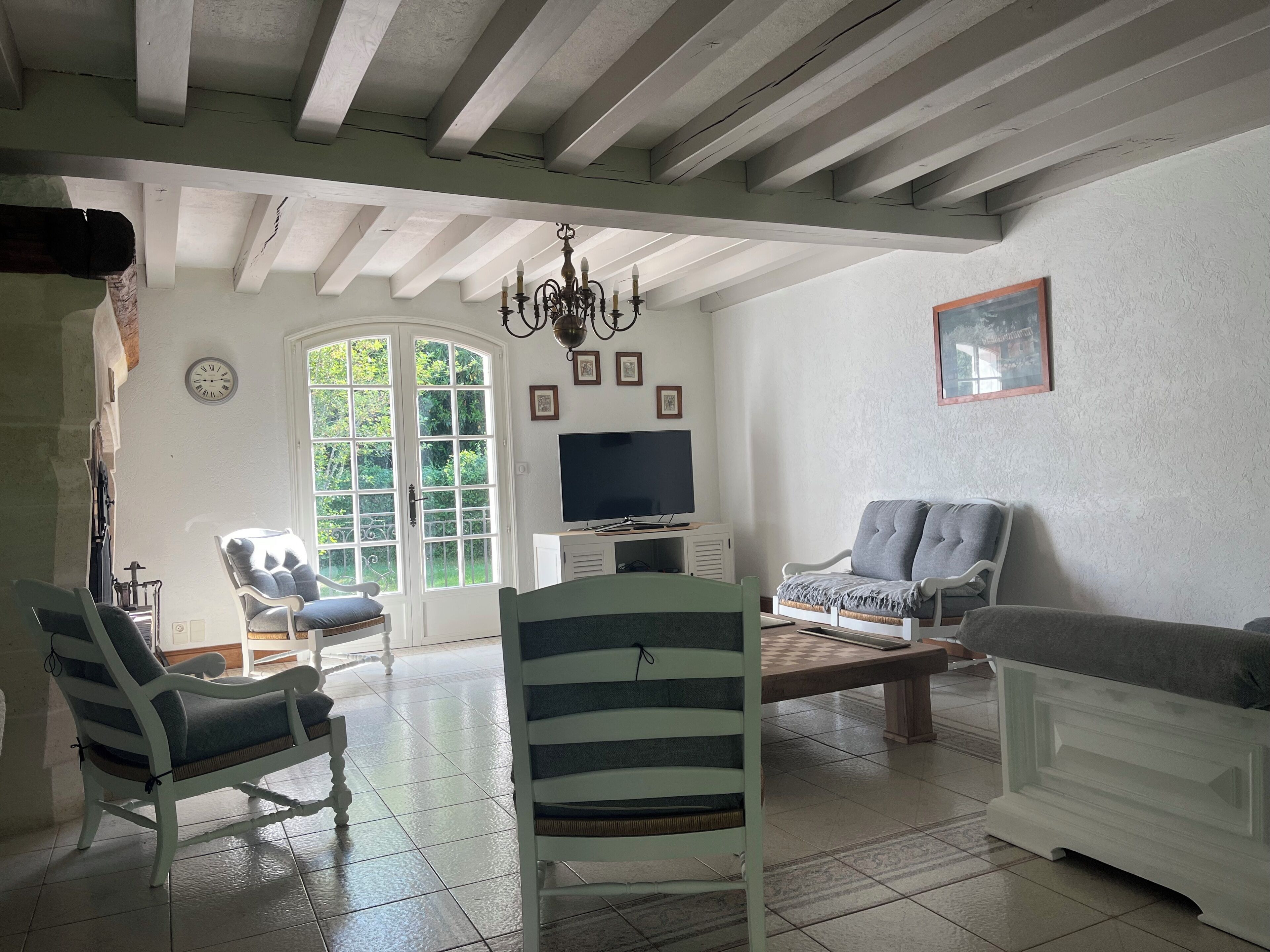 Un ampio soggiorno con soffitto alto, un lampadario, una televisione e una grande finestra vista su spazi verdi.
