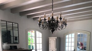 A spacious dining area with a large wooden table and benches, a chandelier, and a view of the outdoors through large windows. - GÎTE LE CATALPA REGION OF THE HIGH LIMOUSIN (Saint-Georges-Les-Landes)