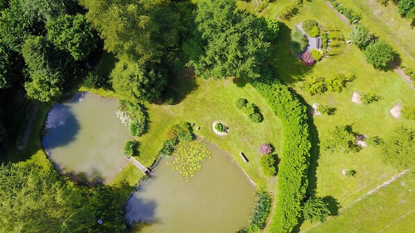 An aerial view of a park with a pond, pathways, and various trees.