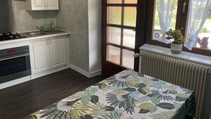 A kitchen with white cabinets, a stove, and a window with a plant. - Gite Les Marmottes Stage & stay (La Salle)
