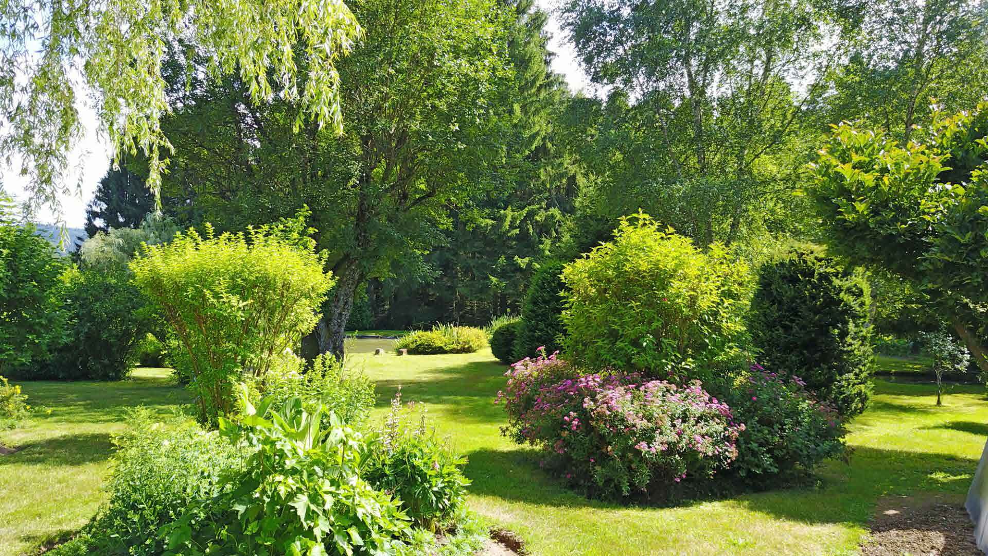 Een weelderige tuin met verschillende bomen en struiken, een verzorgd gazon en een kleine vijver.