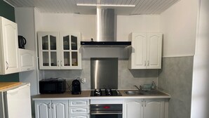 A modern kitchen with white cabinetry, a stainless steel range hood, a built-in oven, and a coffee maker. - Gite Les Marmottes Stage & stay (La Salle)