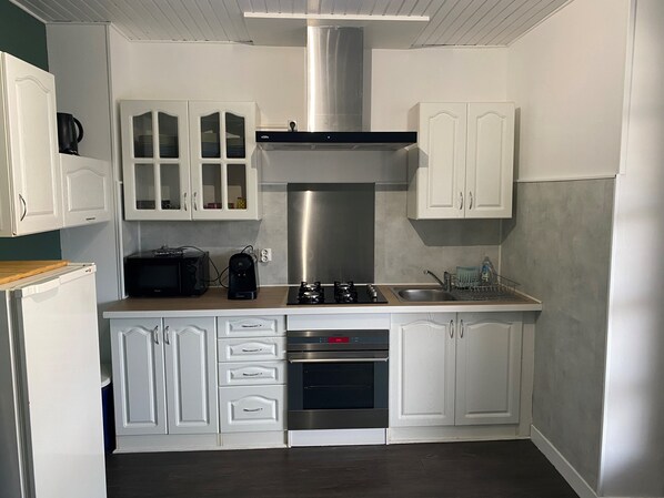 A modern kitchen with white cabinetry, a stainless steel range hood, a built-in oven, and a coffee maker.