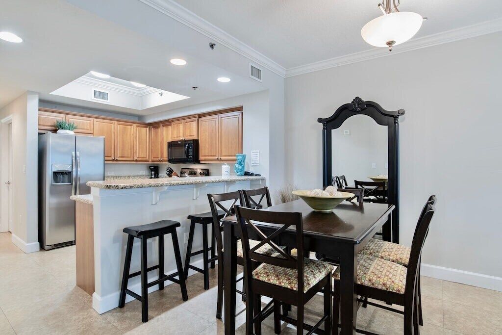 A modern kitchen with wooden cabinets, a central island, and a dining area with dark wooden chairs and a large bowl on the table.