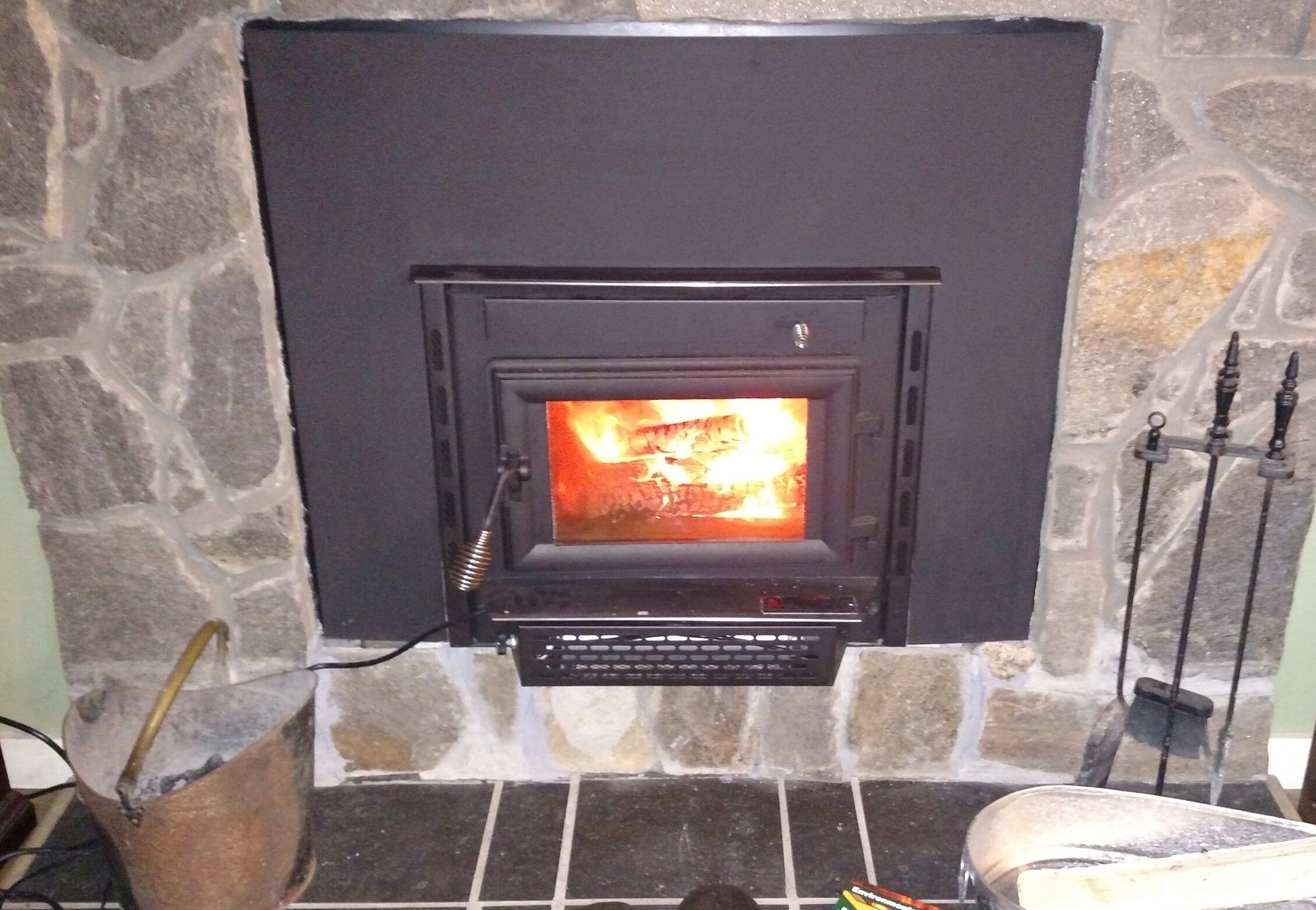A stone fireplace with a black front panel and a visible fire inside.