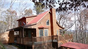 A wooden cabin with a red roof, a deck, and a stone pathway leading to the entrance.
