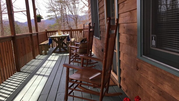 A wooden deck with rocking chairs and a table, overlooking a mountainous landscape.