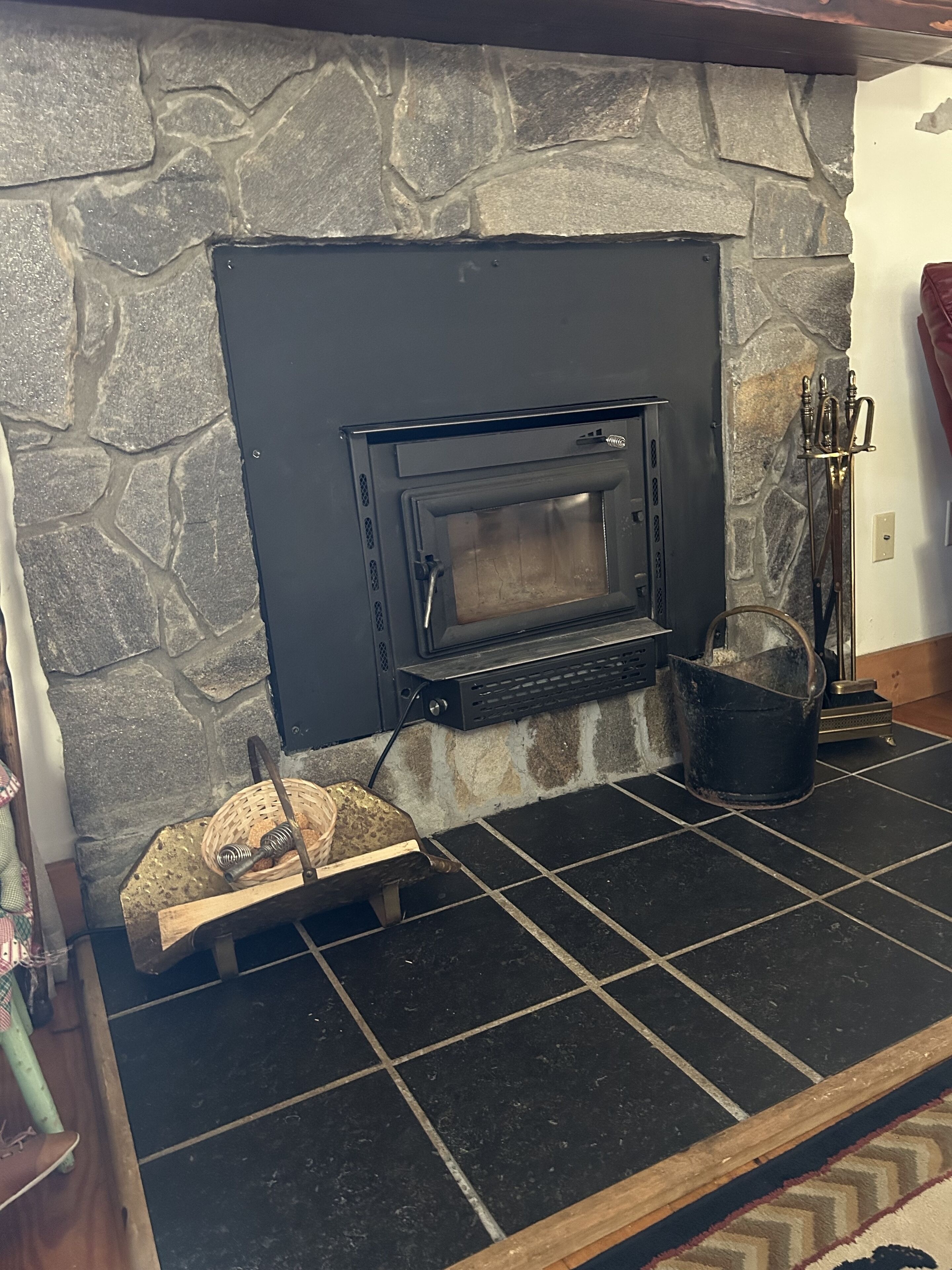 Una chimenea de piedra con estufa eléctrica moderna, un banco de madera y un cubo de metal.