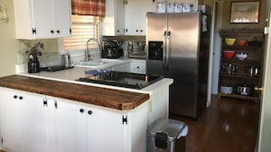 A kitchen with white cabinets, a stainless steel refrigerator, a wooden countertop, and a sink.