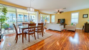 A spacious living room with a dining area, large windows, and a ceiling fan.