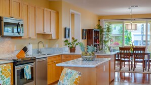 A kitchen with wooden cabinets, a microwave, a sink, and a dining area with chairs and a table.