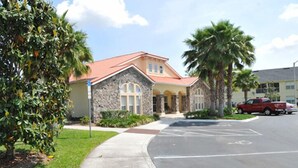 A building with a stone facade and a red roof, surrounded by palm trees and a parking lot. - Club Cortile Resort #1 - 4 Bed 3 Baths Townhome (Kissimmee)