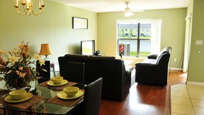 A dining area with a glass table, chairs, and a vase of flowers. There is a black sofa and a black armchair in the background. - Club Cortile Resort #1 - 4 Bed 3 Baths Townhome (Kissimmee)