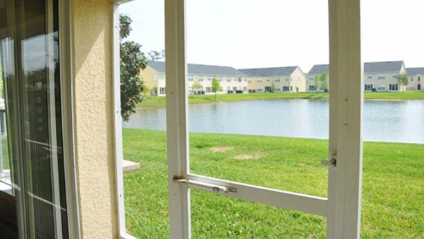 A view through a glass door of a building with a grassy area and a body of water in the background. - Club Cortile Resort #1 - 4 Bed 3 Baths Townhome (Kissimmee)