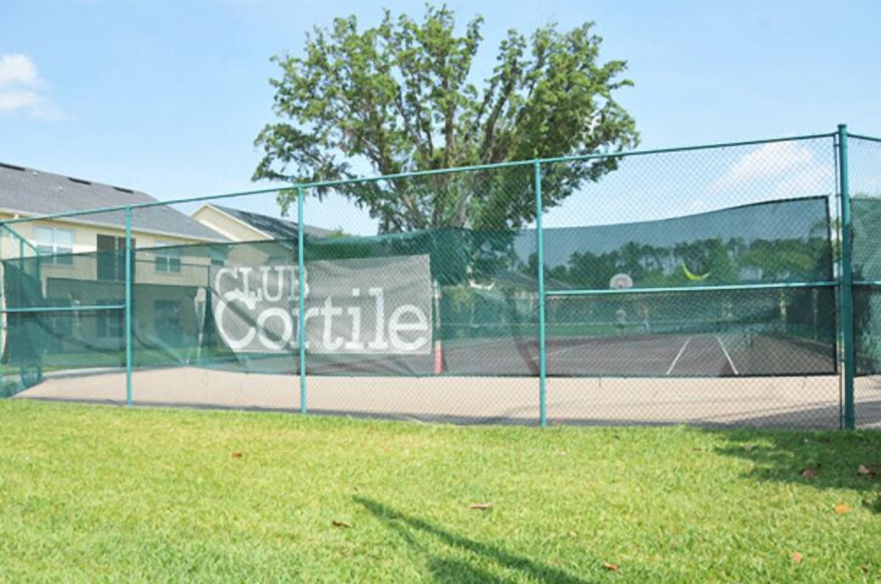A tennis court enclosed by a green fence with a sign reading "Club Cortile".
