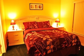 A bed with a floral bedspread, two bedside lamps, a nightstand, and a framed picture on the wall.
