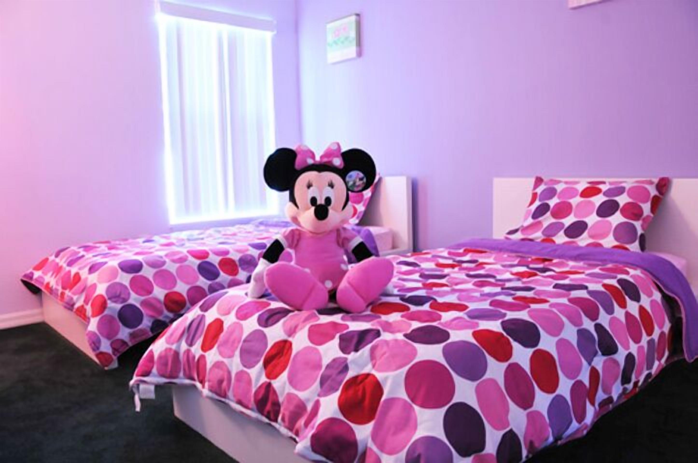 A bedroom with two beds, each with a polka dot bedspread, a Minnie Mouse plush toy on the left bed, and a window with blinds.