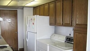 A compact kitchen with wooden cabinets, a white refrigerator, a washing machine, and a stove. - Cottage by the Sea - Ocean Front (Yachats)