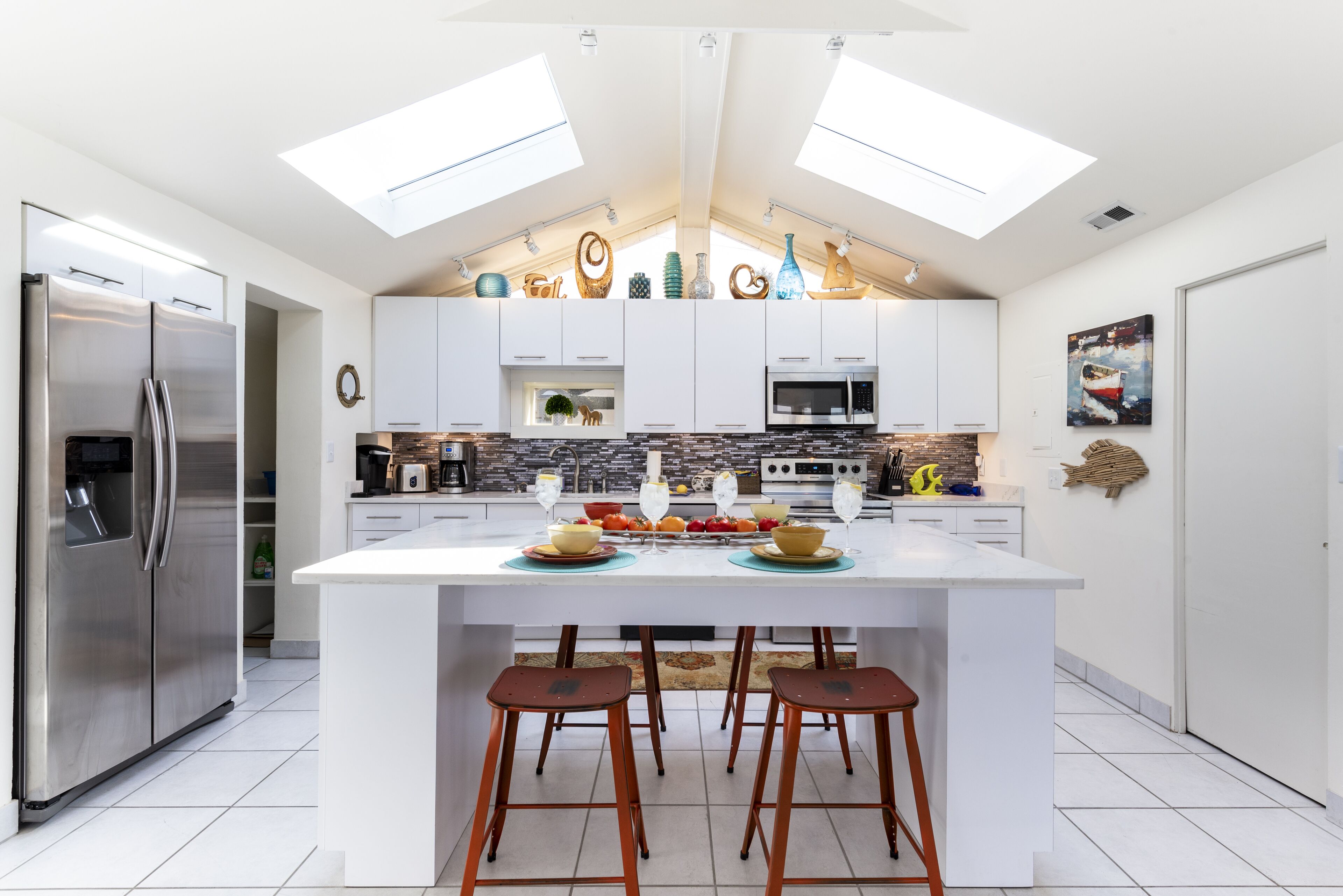 A modern kitchen with a central island, stainless steel appliances, and skylights.