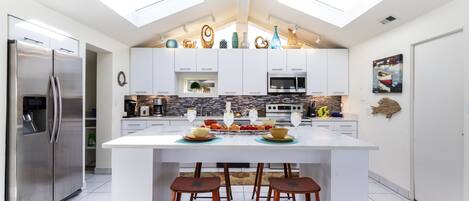A modern kitchen with a central island, stainless steel appliances, and skylights.
