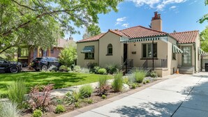 A two-story house with a red-tiled roof, a front porch with a striped awning, and a well-maintained garden with various plants and a lawn. - Park Hill Holly House - A Place To Call Home  
License: 2018-BFN-0000208 (Denver)