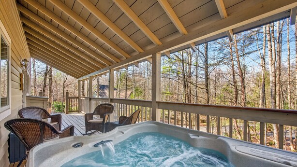 Ein Whirlpool mit Holzterrasse und Korbstühlen, umgeben von einem Holgitter und Bäumen.