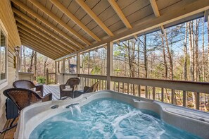 Ein Whirlpool mit Holzterrasse und Korbstühlen, umgeben von einem Holgitter und Bäumen.